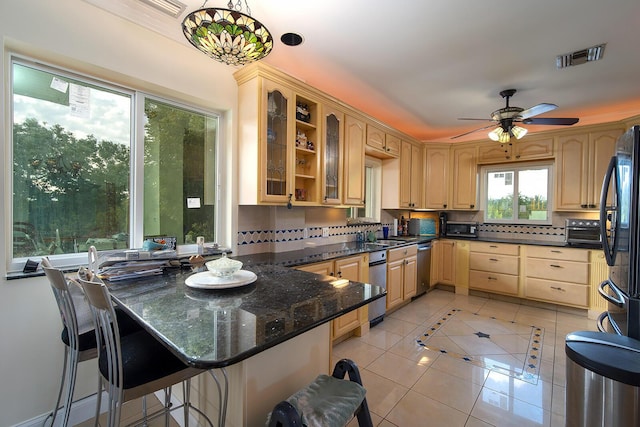 kitchen featuring light tile patterned floors, glass insert cabinets, dark stone countertops, a peninsula, and pendant lighting