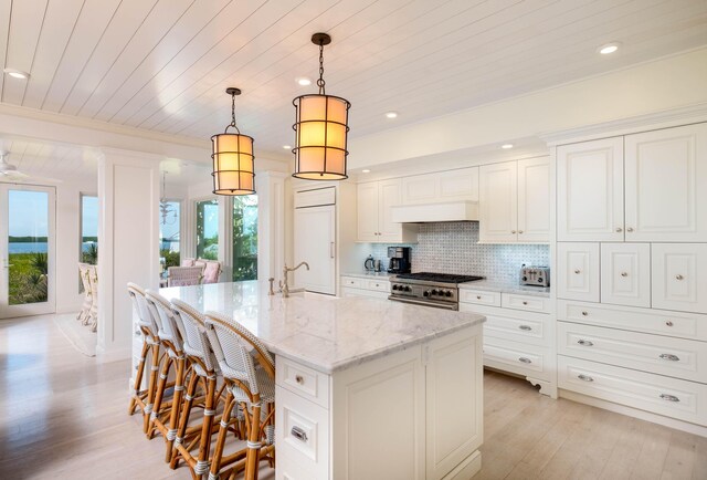 kitchen with white cabinetry, stainless steel range, pendant lighting, light stone countertops, and a kitchen island with sink