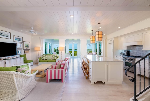 kitchen with light stone counters, tasteful backsplash, high end stove, white cabinets, and decorative light fixtures