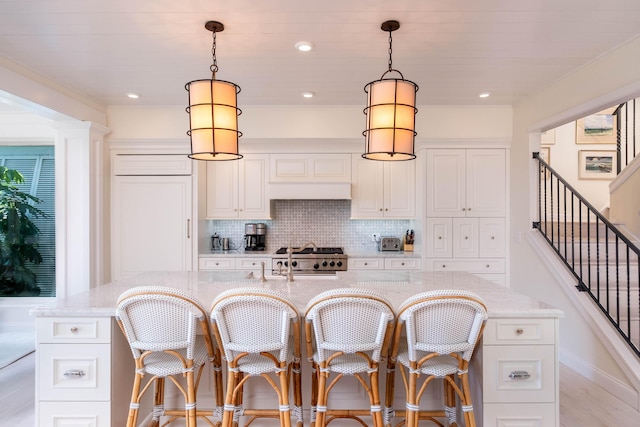 kitchen with white cabinetry, hanging light fixtures, light stone countertops, and an island with sink