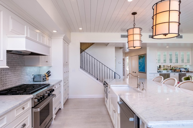 kitchen with pendant lighting, stainless steel appliances, white cabinets, and a center island with sink