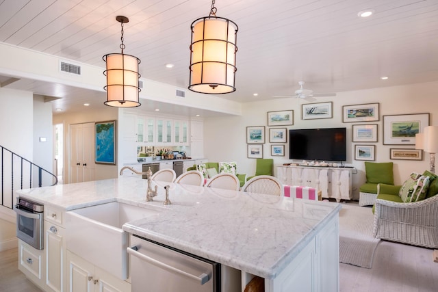 kitchen with white cabinetry, stainless steel appliances, light stone counters, a center island with sink, and decorative light fixtures