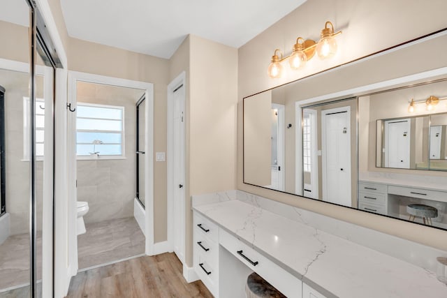 full bathroom featuring hardwood / wood-style flooring, vanity, bath / shower combo with glass door, and toilet