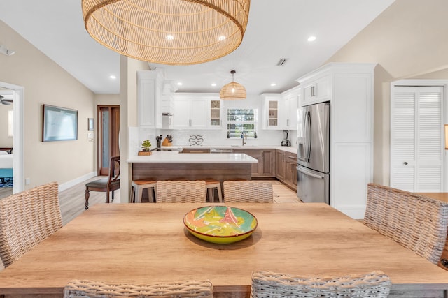 kitchen featuring lofted ceiling, sink, stainless steel fridge with ice dispenser, kitchen peninsula, and white cabinets