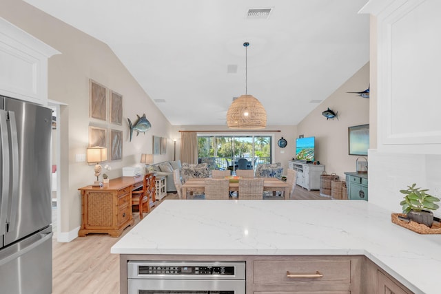 kitchen featuring white cabinets, hanging light fixtures, stainless steel fridge, and light stone counters