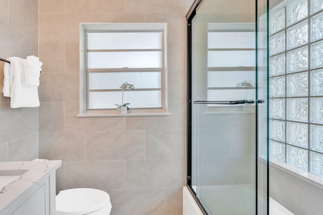 full bathroom featuring vanity, combined bath / shower with glass door, tile walls, and toilet