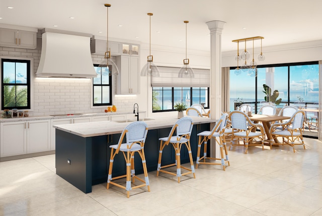 kitchen with premium range hood, white cabinetry, light stone countertops, and a center island with sink