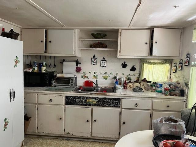 kitchen with black microwave, a sink, light countertops, open shelves, and white cabinetry