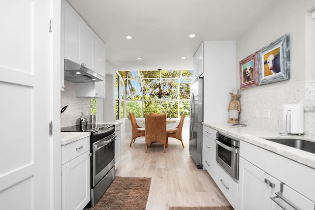 kitchen featuring light wood-type flooring, white cabinets, pendant lighting, stainless steel appliances, and backsplash