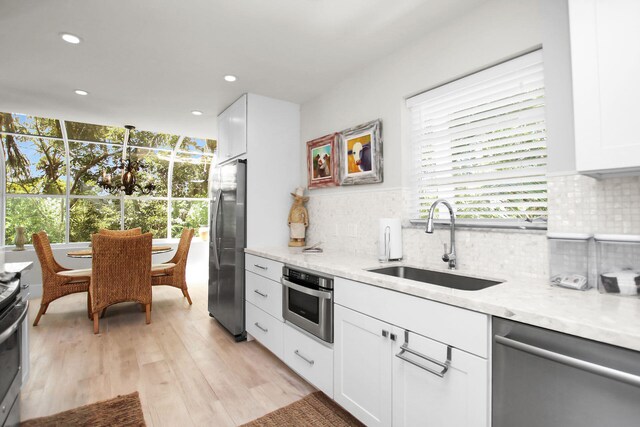 kitchen with appliances with stainless steel finishes, a wealth of natural light, white cabinetry, sink, and light stone counters