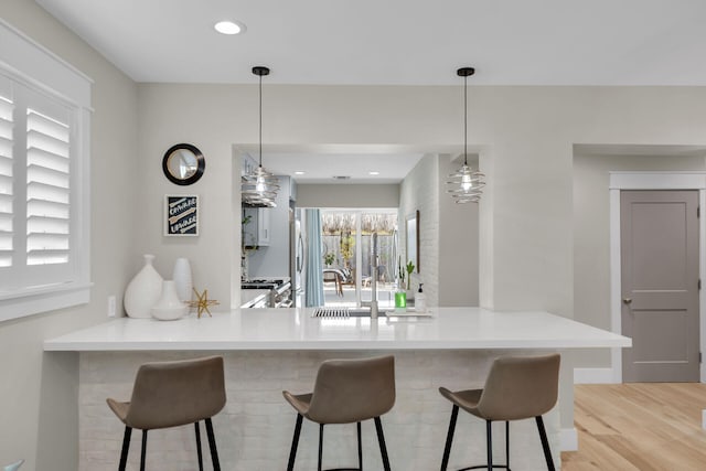 122 S Bay Harbor Dr, Key Largo, FL 33037 - kitchen with a peninsula, light wood-style flooring, a kitchen bar, appliances with stainless steel finishes, and hanging light fixtures
