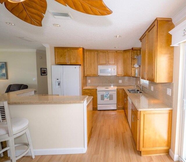 kitchen with a breakfast bar, sink, decorative backsplash, light hardwood / wood-style floors, and white appliances