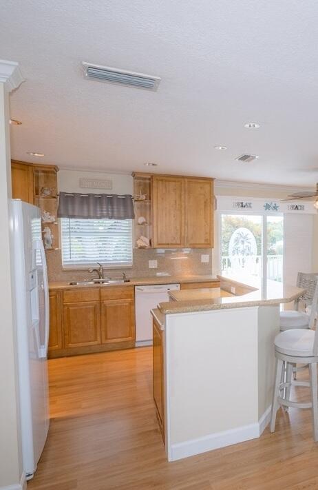 kitchen with sink, a breakfast bar area, light wood-type flooring, white appliances, and decorative backsplash