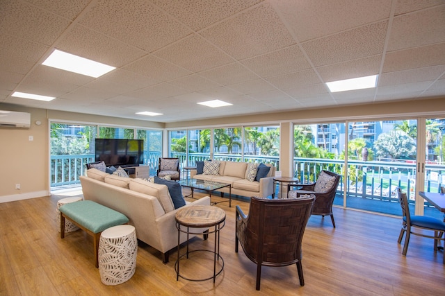 living room with a healthy amount of sunlight, a wall mounted air conditioner, a drop ceiling, and light hardwood / wood-style flooring