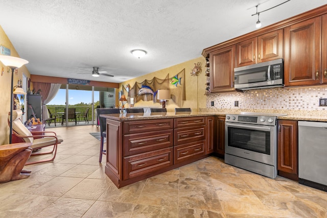 kitchen featuring light stone counters, a textured ceiling, kitchen peninsula, stainless steel appliances, and backsplash