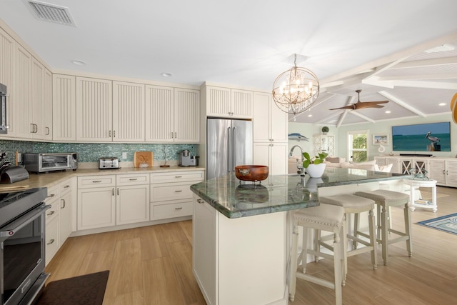 kitchen featuring high end fridge, tasteful backsplash, range, hanging light fixtures, and an island with sink