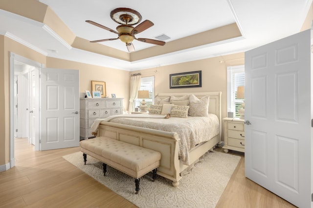 bedroom featuring a tray ceiling, ornamental molding, light hardwood / wood-style floors, and ceiling fan