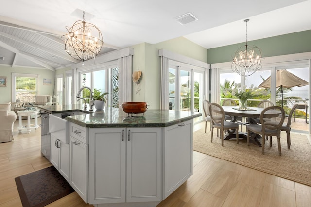 kitchen with plenty of natural light, a chandelier, a kitchen island with sink, and hanging light fixtures