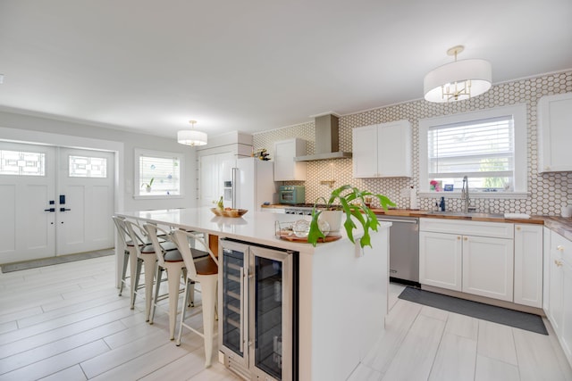 kitchen featuring wine cooler, wall chimney range hood, decorative light fixtures, and white cabinets