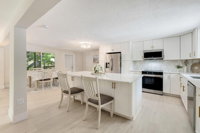 82260 Overseas Hwy, Islamorada, FL 33036 - kitchen with stainless steel appliances, light wood-style floors, a kitchen island, tasteful backsplash, and a textured ceiling