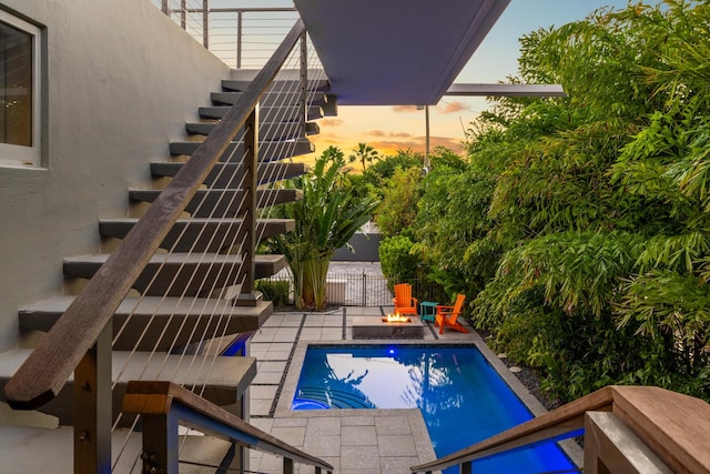 pool at dusk with a patio area and a fire pit