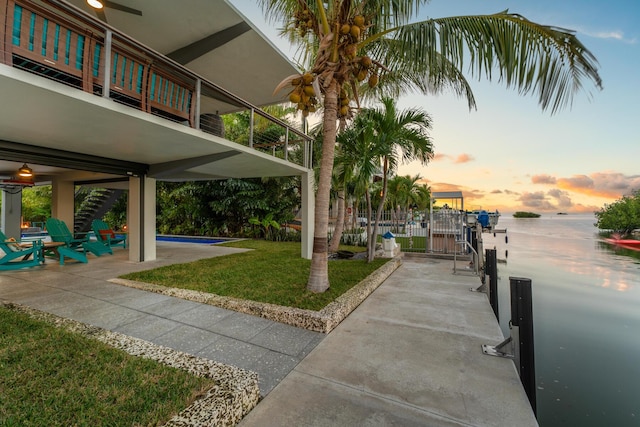 exterior space with a patio area, a dock, a lawn, and a water view