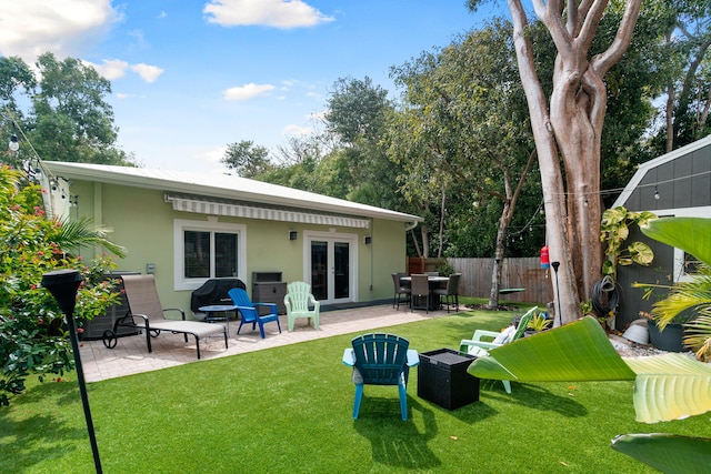 rear view of property with stucco siding, a lawn, a patio, fence, and french doors