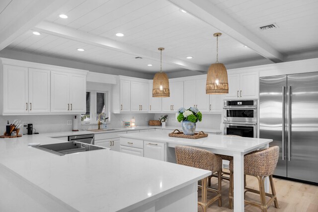 kitchen with appliances with stainless steel finishes, pendant lighting, white cabinetry, a kitchen bar, and beam ceiling