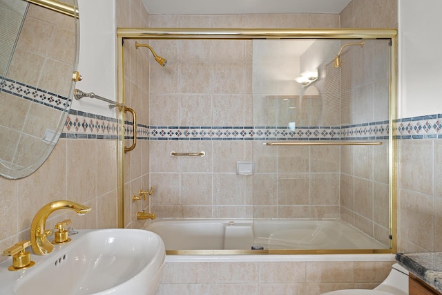 bathroom featuring tile walls, combined bath / shower with glass door, and sink