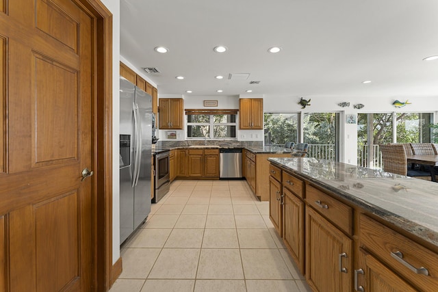 kitchen featuring dark stone counters, light tile patterned flooring, stainless steel appliances, and a healthy amount of sunlight