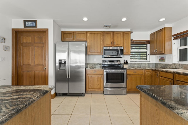 kitchen with sink, appliances with stainless steel finishes, dark stone countertops, and light tile patterned floors