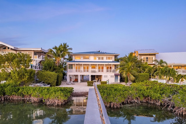 back of house featuring a patio, a water view, a balcony, and solar panels