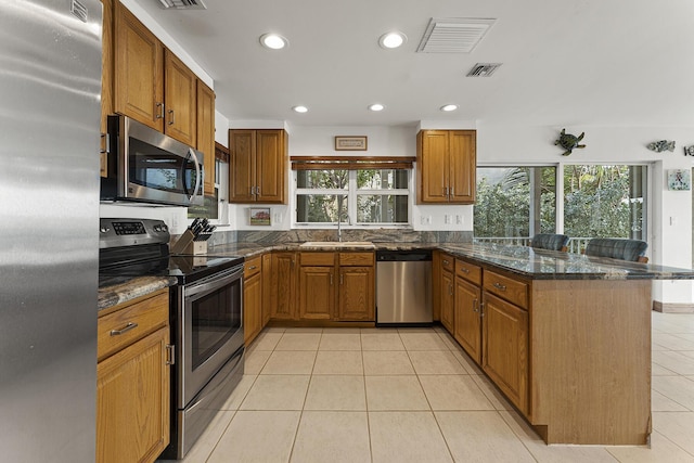 kitchen with kitchen peninsula, stainless steel appliances, sink, light tile patterned floors, and dark stone counters