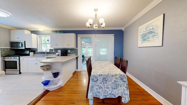 kitchen featuring white cabinetry, crown molding, an inviting chandelier, pendant lighting, and stainless steel appliances