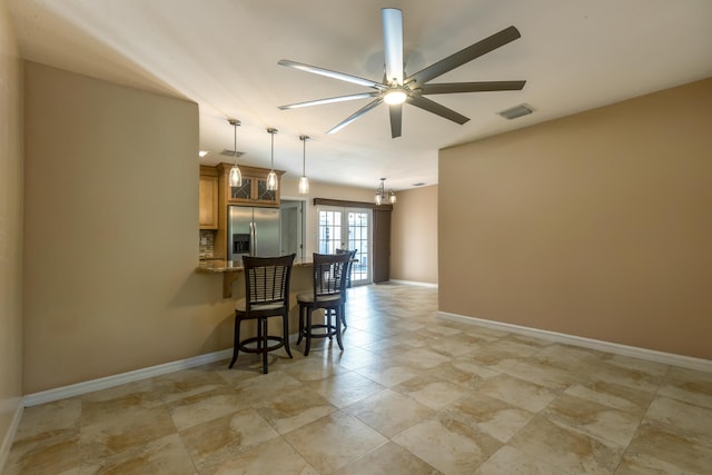 kitchen featuring stainless steel refrigerator with ice dispenser, a breakfast bar, light stone counters, decorative light fixtures, and ceiling fan with notable chandelier