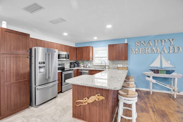 kitchen with sink, a breakfast bar area, light stone counters, stainless steel appliances, and backsplash