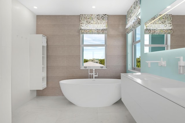 bathroom with tile walls, a bath, and vanity