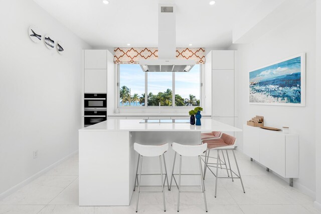 kitchen featuring white cabinetry, multiple ovens, a breakfast bar, and island exhaust hood