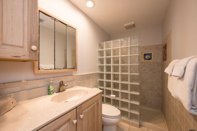 bathroom featuring tile walls, tile patterned flooring, vanity, tiled shower, and toilet