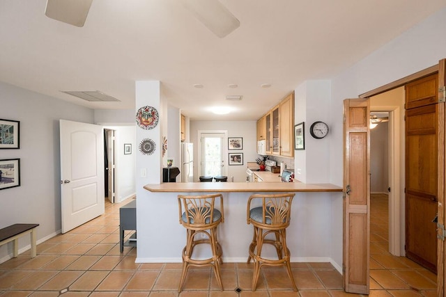 kitchen with a breakfast bar area, white appliances, light tile patterned floors, and kitchen peninsula