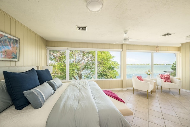 bedroom featuring light tile patterned flooring, a water view, and a textured ceiling