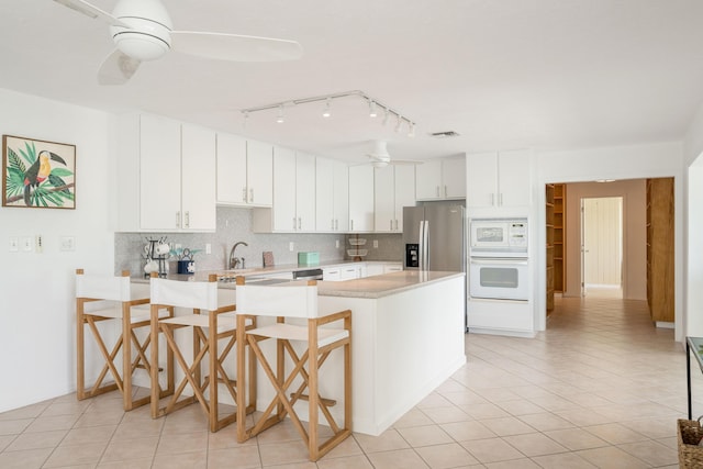 kitchen featuring a breakfast bar area, white cabinets, ceiling fan, kitchen peninsula, and white appliances