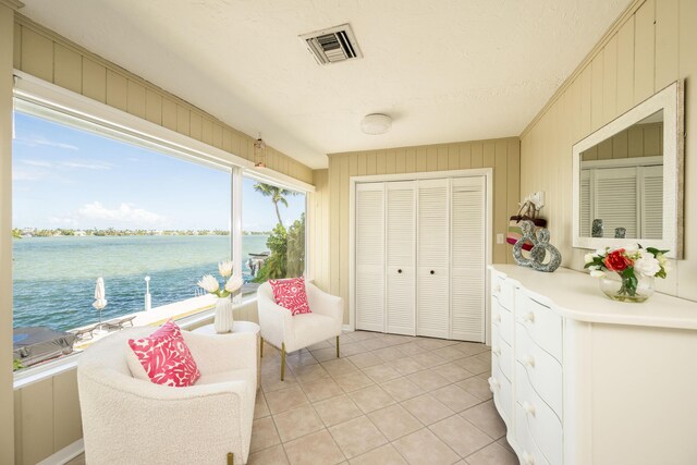 living area with wooden walls, light tile patterned flooring, a textured ceiling, and a water view