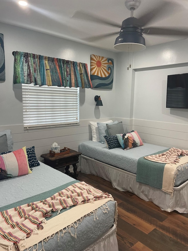 bedroom featuring ceiling fan, wainscoting, wood finished floors, and wooden walls