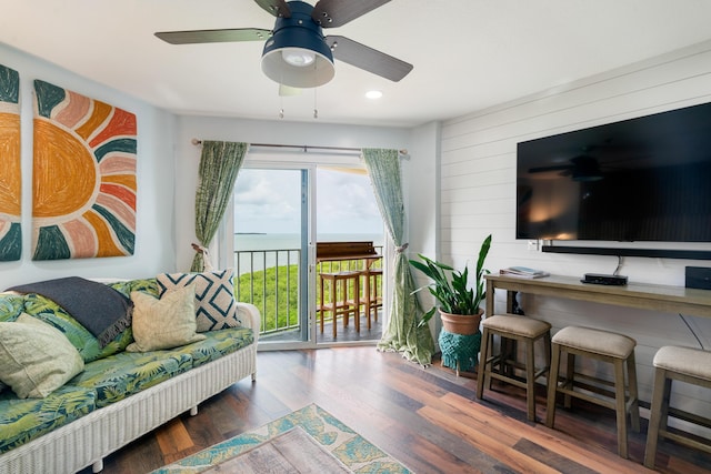 living room with ceiling fan, wooden walls, and wood finished floors