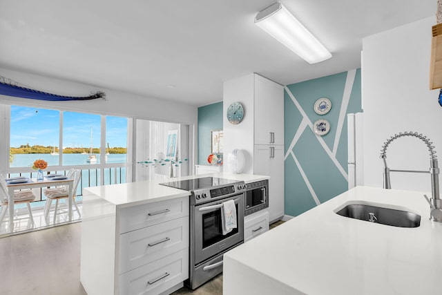 kitchen featuring sink, appliances with stainless steel finishes, a water view, white cabinets, and light wood-type flooring