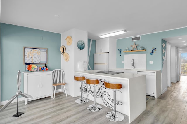 kitchen with sink, white appliances, light hardwood / wood-style floors, white cabinets, and kitchen peninsula