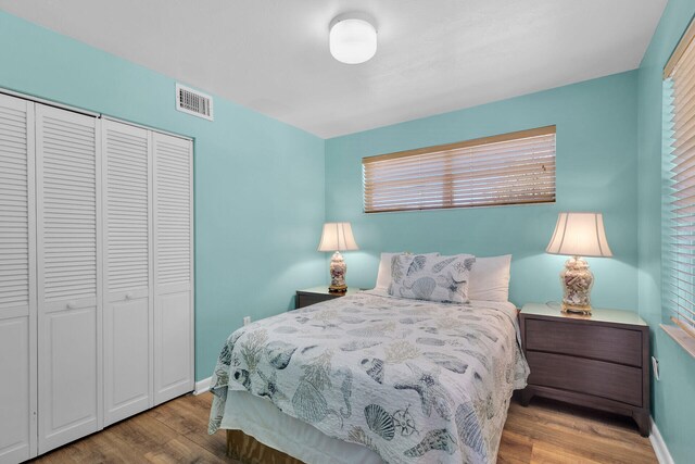 bedroom with a closet, visible vents, baseboards, and wood finished floors