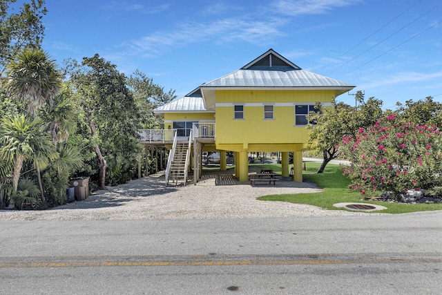 coastal inspired home featuring driveway, a front lawn, stairway, a fire pit, and a carport