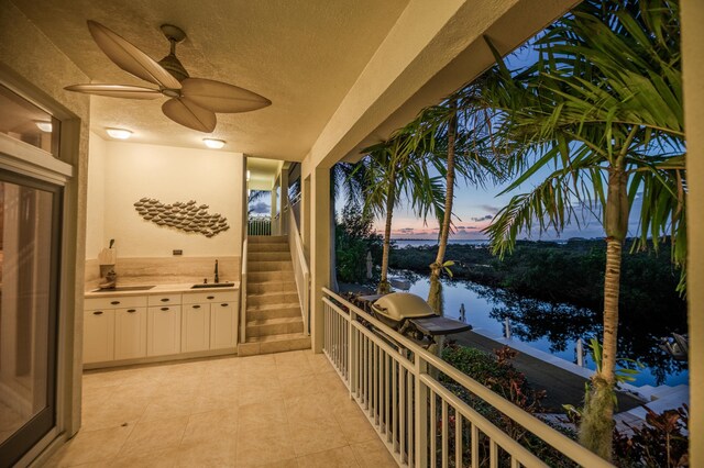 balcony at dusk featuring a water view, ceiling fan, and sink